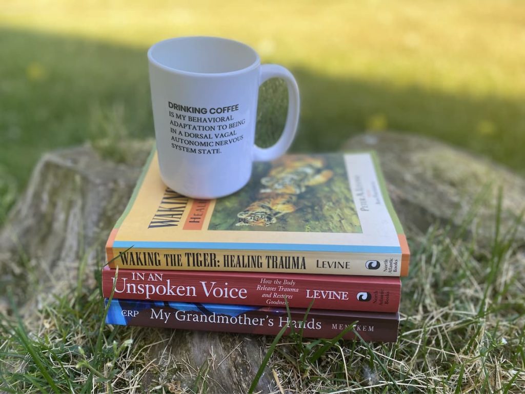 A cup of coffee sits on three books about healing trauma.